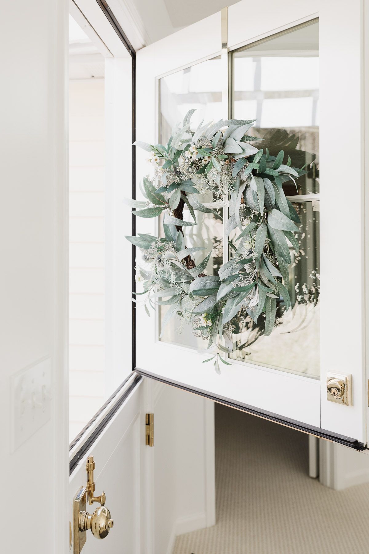 A year-round front door garland with gray-green color on the white door.