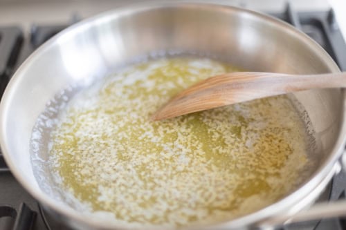 Melted butter in a stainless steel pan being stirred with a wooden spoon on a stovetop, transforming into a rich garlic parmesan sauce.