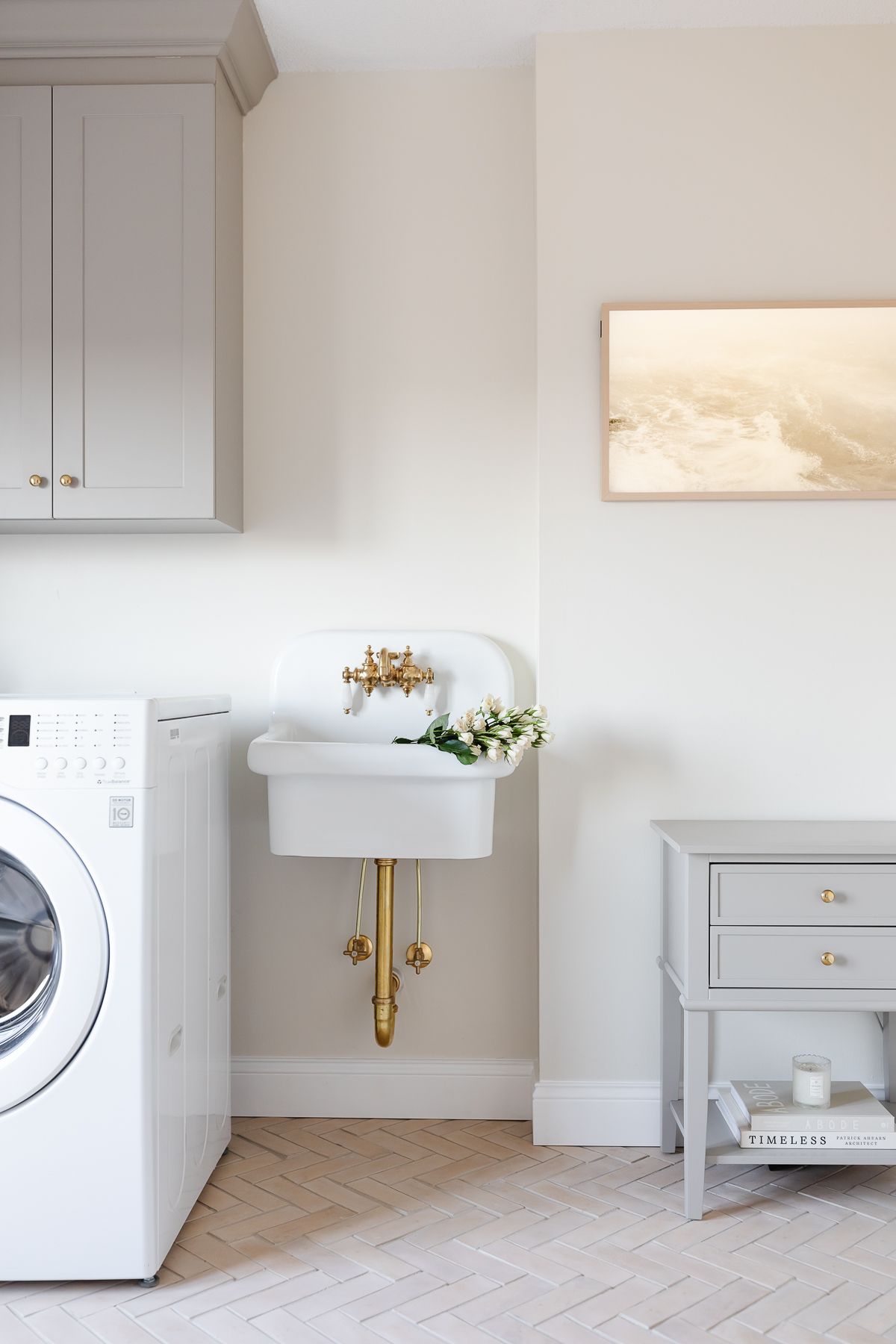 The laundry room has gray cabinets, wall sink and herringbone floor.