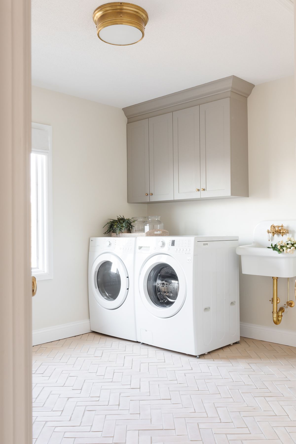 The laundry room has gray cabinets, wall sink and herringbone floor.