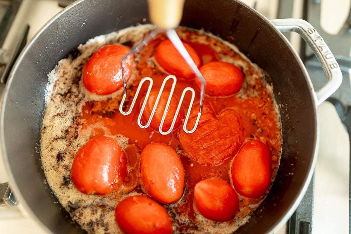 San Marzano tomatoes in a cast iron pan, with a tool beginning to smash them.