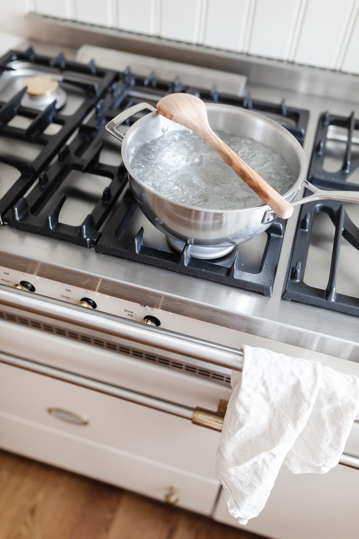 A silver pot of boiling water on the French range, with a wooden spoon placed on top to prevent the water from boiling.