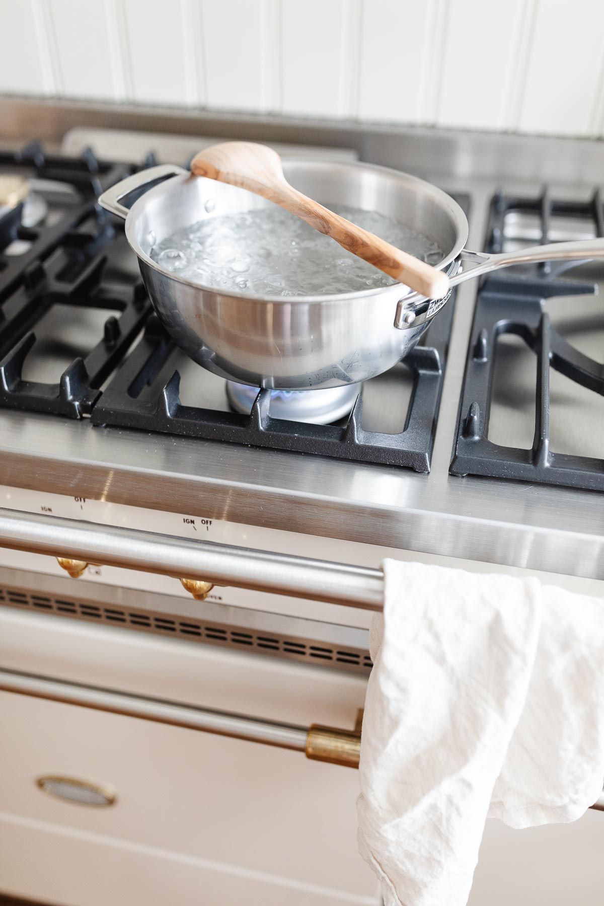 A silver pot of boiling water on a French range, with a wooden spoon placed over the top to stop water from boiling over.