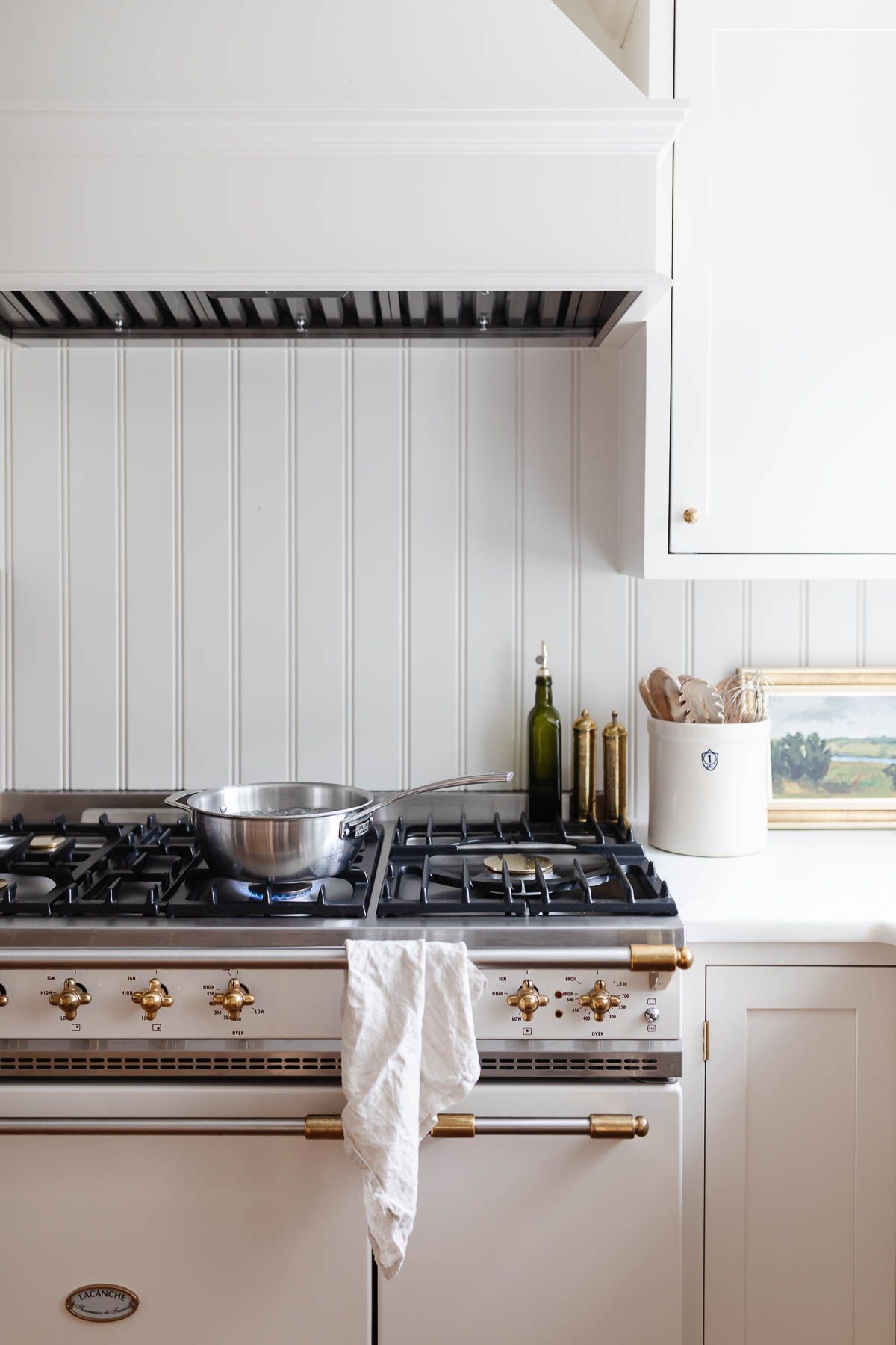 A white kitchen with a silver pot of water boiling on the stove