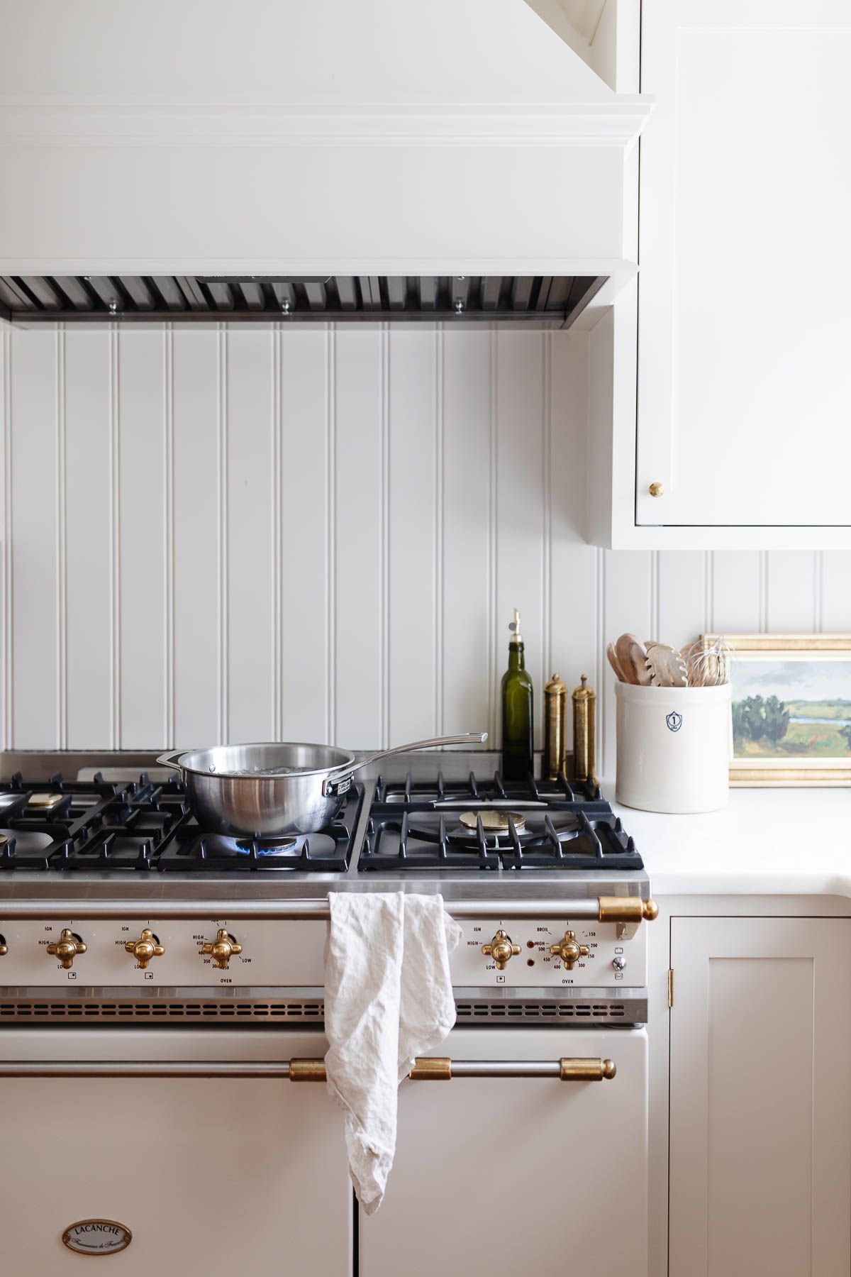 A white kitchen with a silver pot of water boiling on the stove