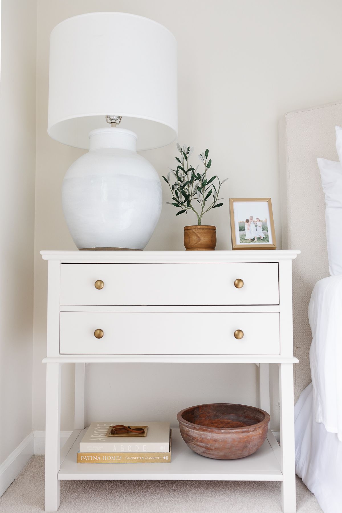 A nightstand decorated with books, lamp, a plant and a picture