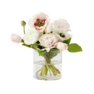 A clear glass vase filled with water holds a bouquet of light pink and white flowers with green leaves, making it a lovely choice for nightstand decorating.
