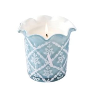 A lit candle in a blue and white ceramic holder with a scalloped edge and white floral pattern, perfect for nightstand decorating.