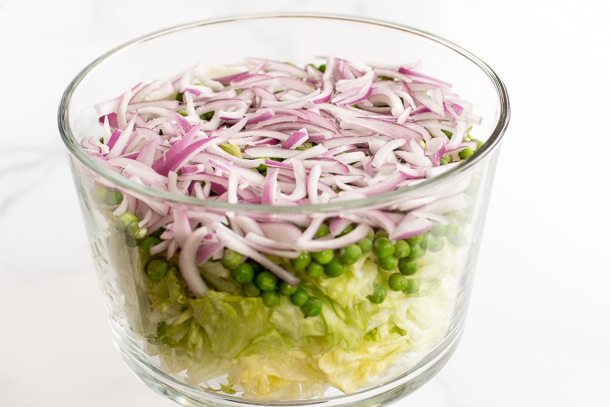 Chopped lettuce topped with peas and onions in a glass serving dish.