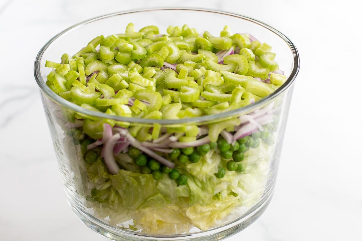 Chopped lettuce topped with peas and onions and celery, in a glass serving dish.