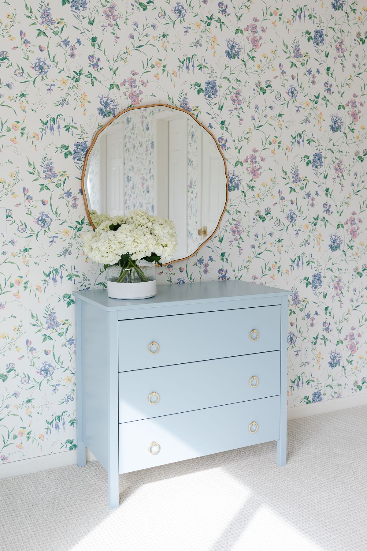 A bedroom with floral wallpaper and painted vanity in blue by Benjamin Moore Slate