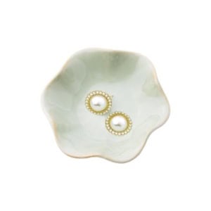 A pair of pearl earrings with gold and small crystal accents rests in a light green, scallop-edged ceramic dish—perfect for effortless nightstand decorating.