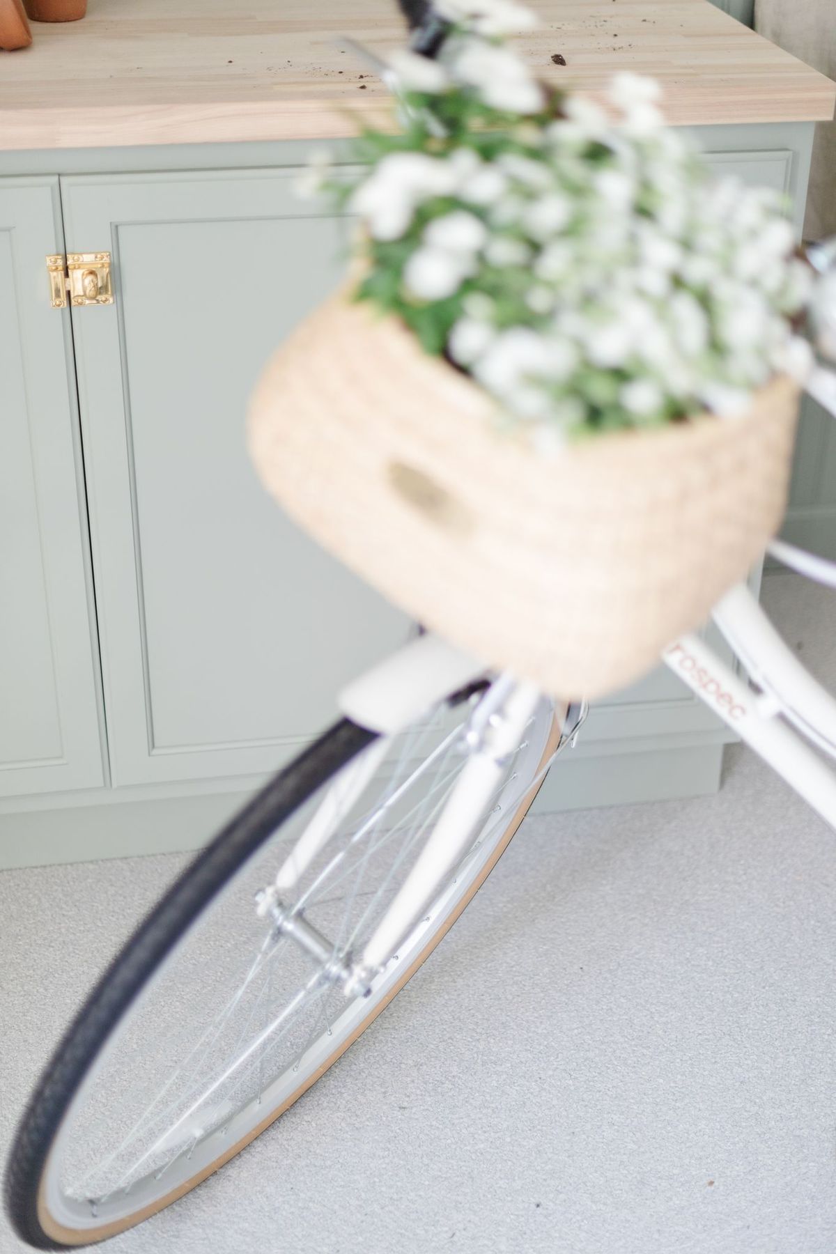 A white bike with a flower basket, in a garage with gray garage floor covering.