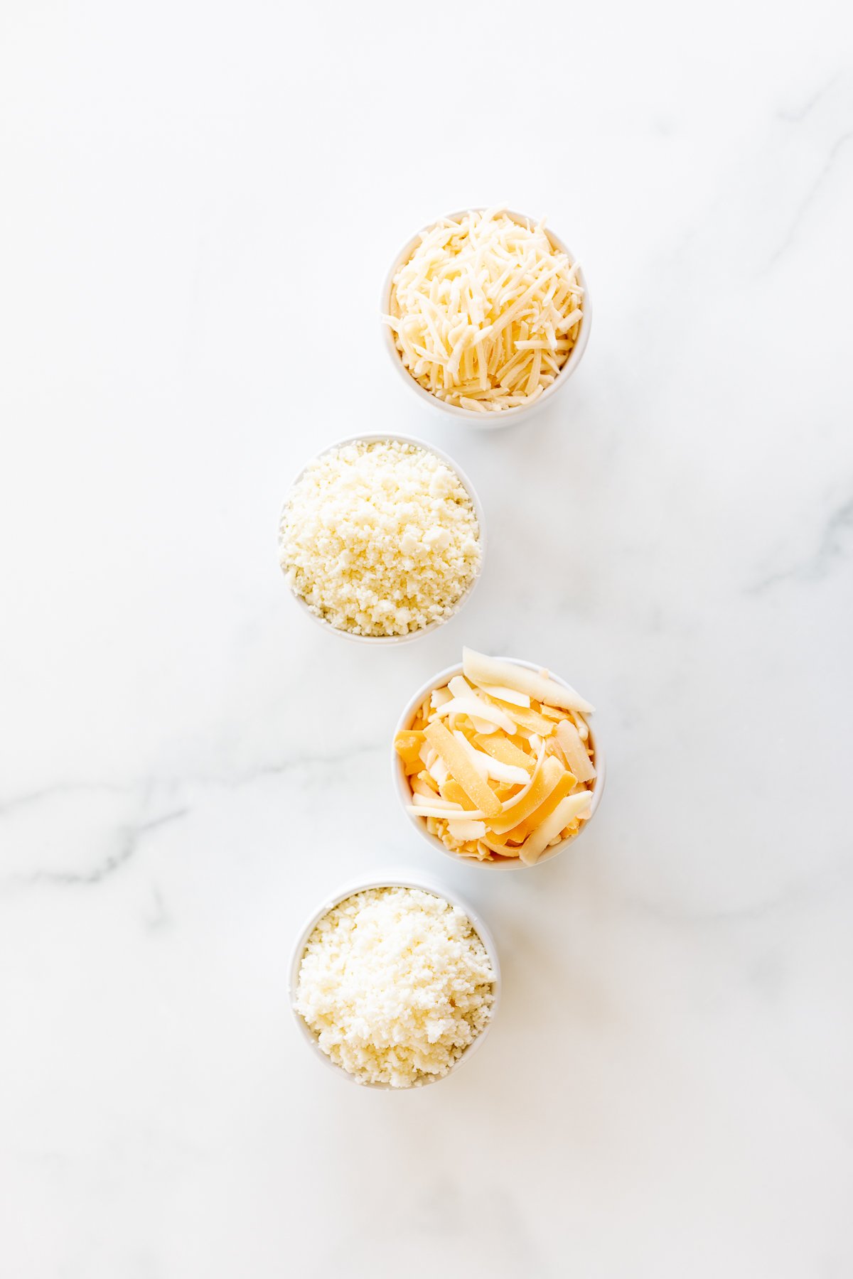 Three bowls of the best cheeses for tacos on a marble surface.