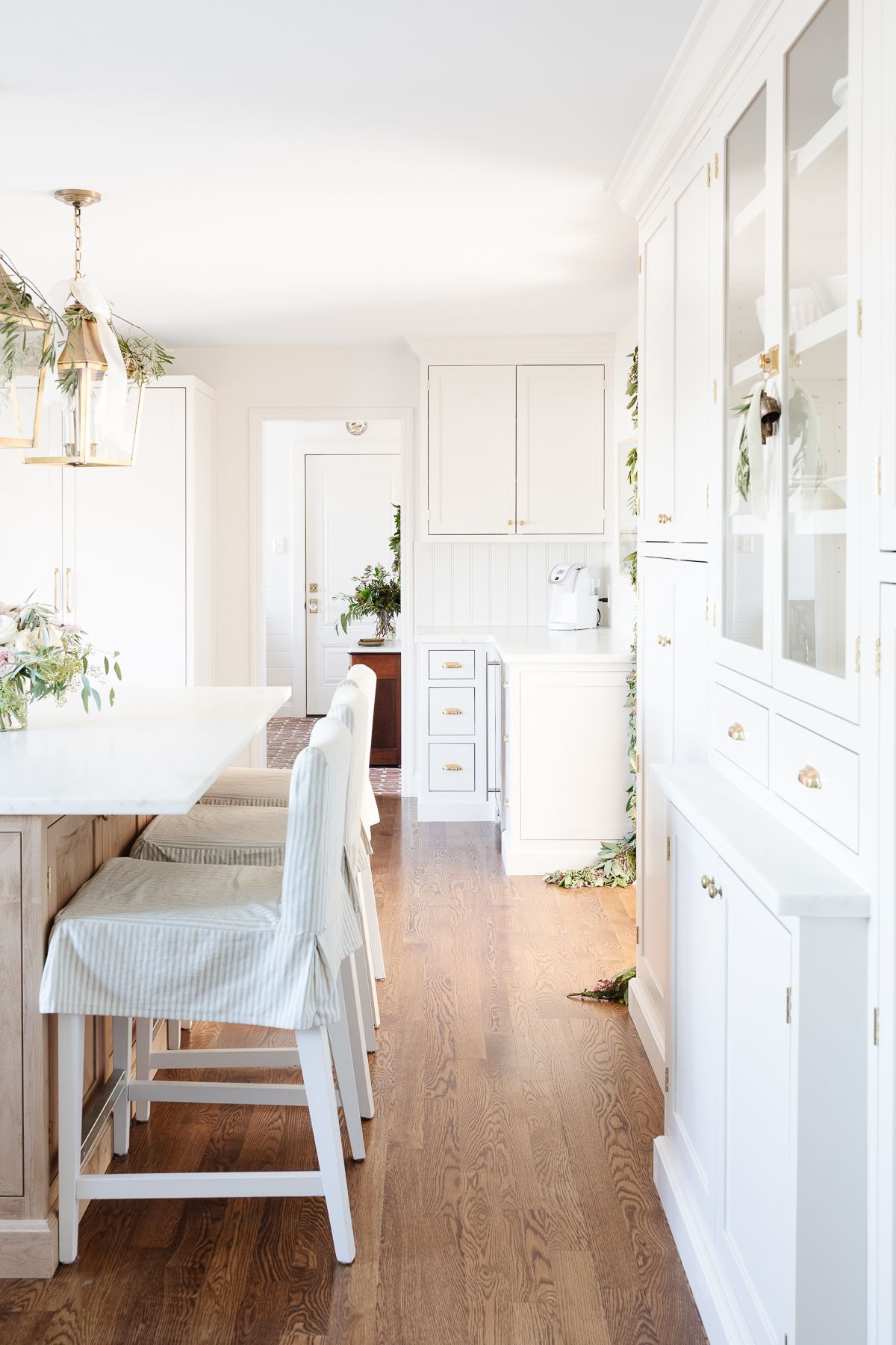 A white kitchen with a wood island and a paneled fridge with brass appliance pulls