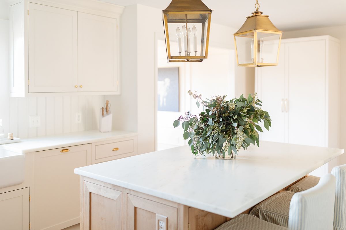 A white kitchen with a wood island and a paneled fridge with brass appliance pulls