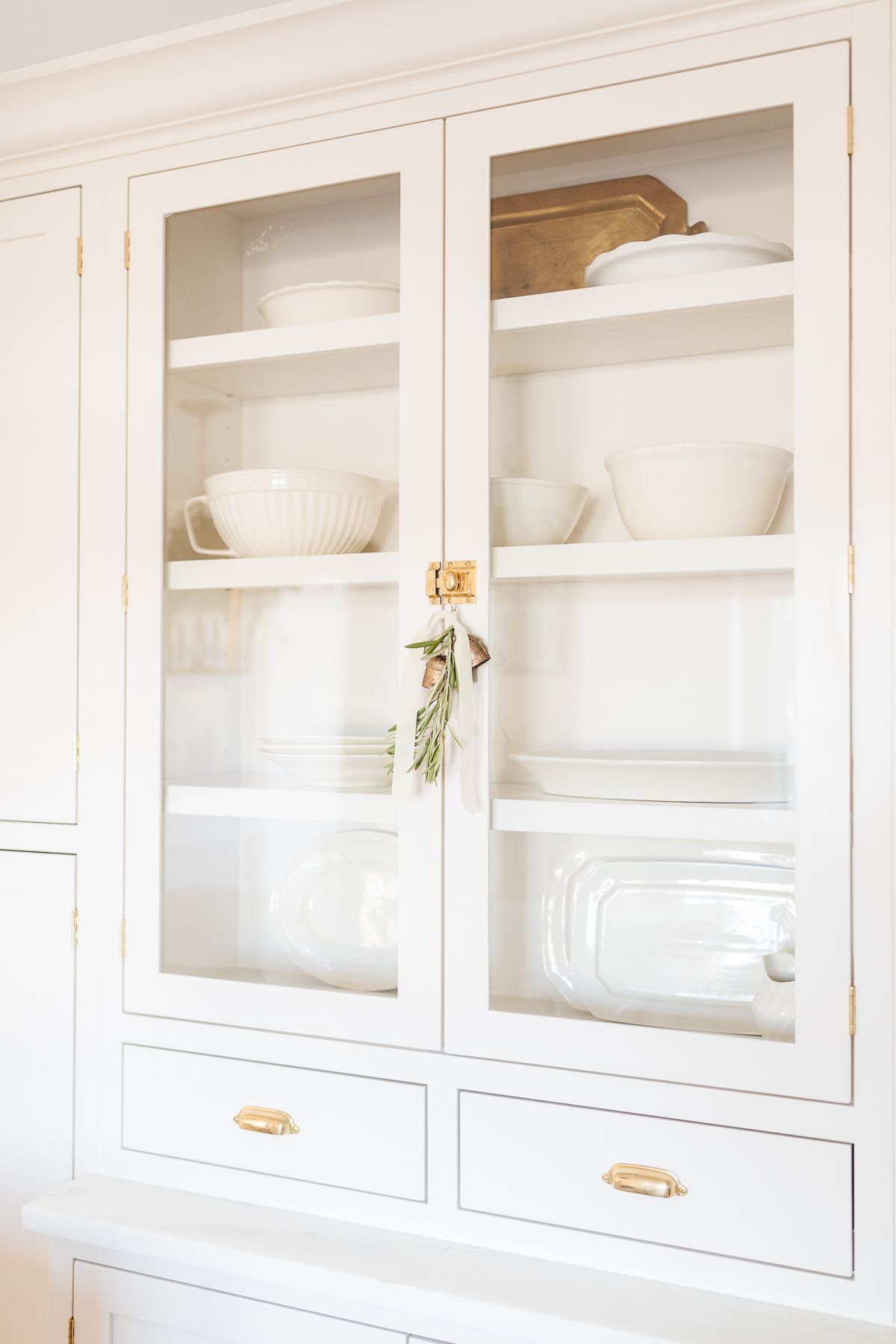 A kitchen cabinet with glass doors and brass cabinet latches