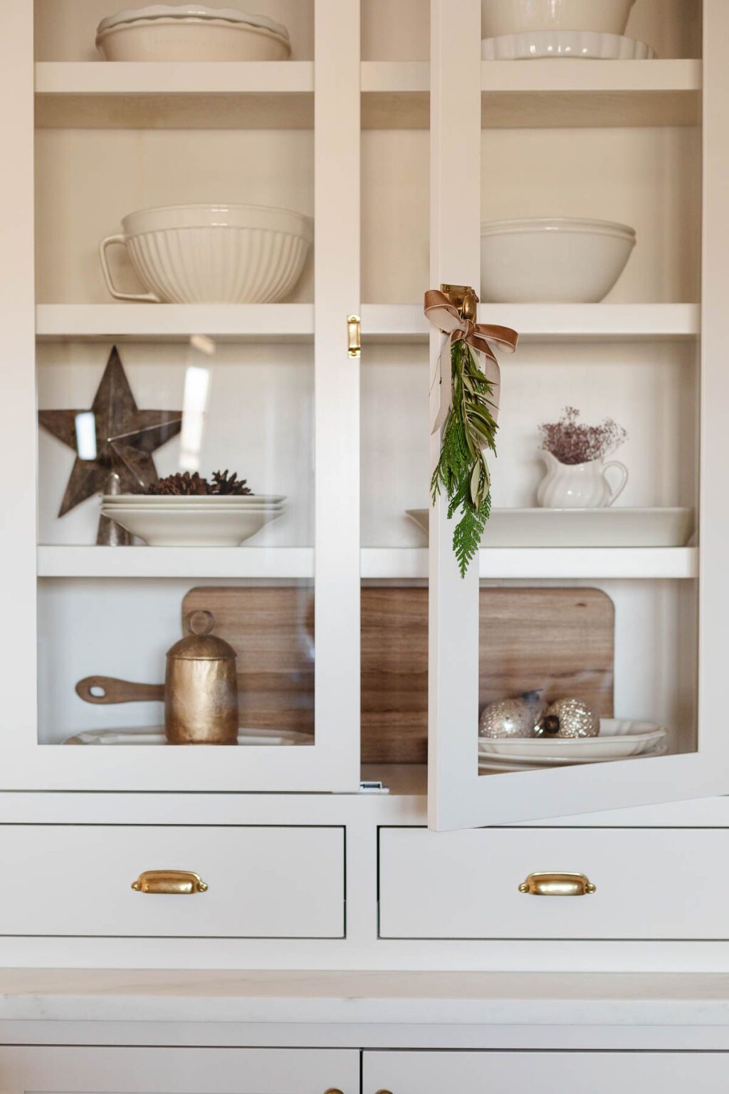 A kitchen cabinet with glass doors and brass cabinet latches