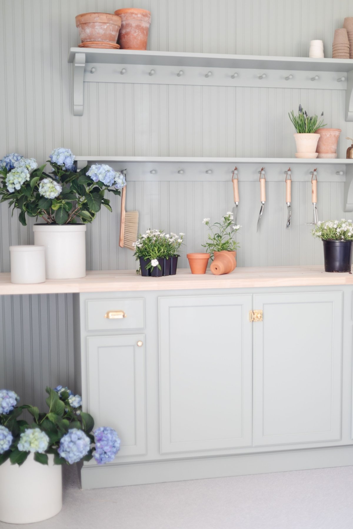 A green potting bench with brass hardware and cabinet latches