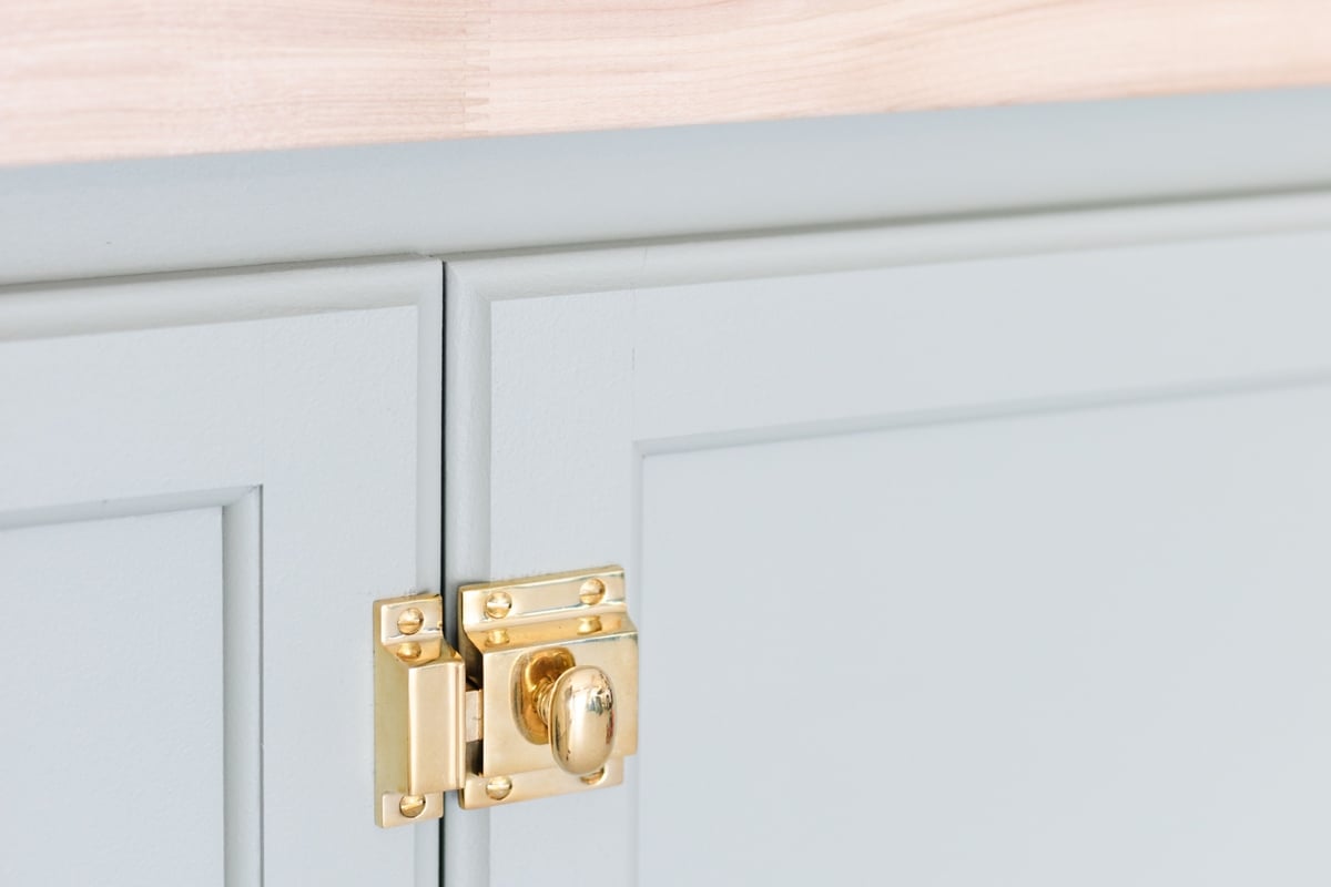 A green potting bench with brass hardware and cabinet latches