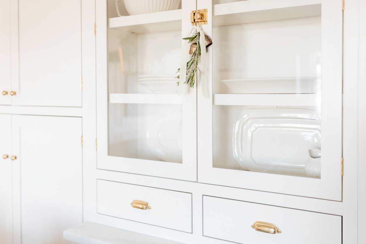 A kitchen cabinet with glass doors and brass cabinet latches