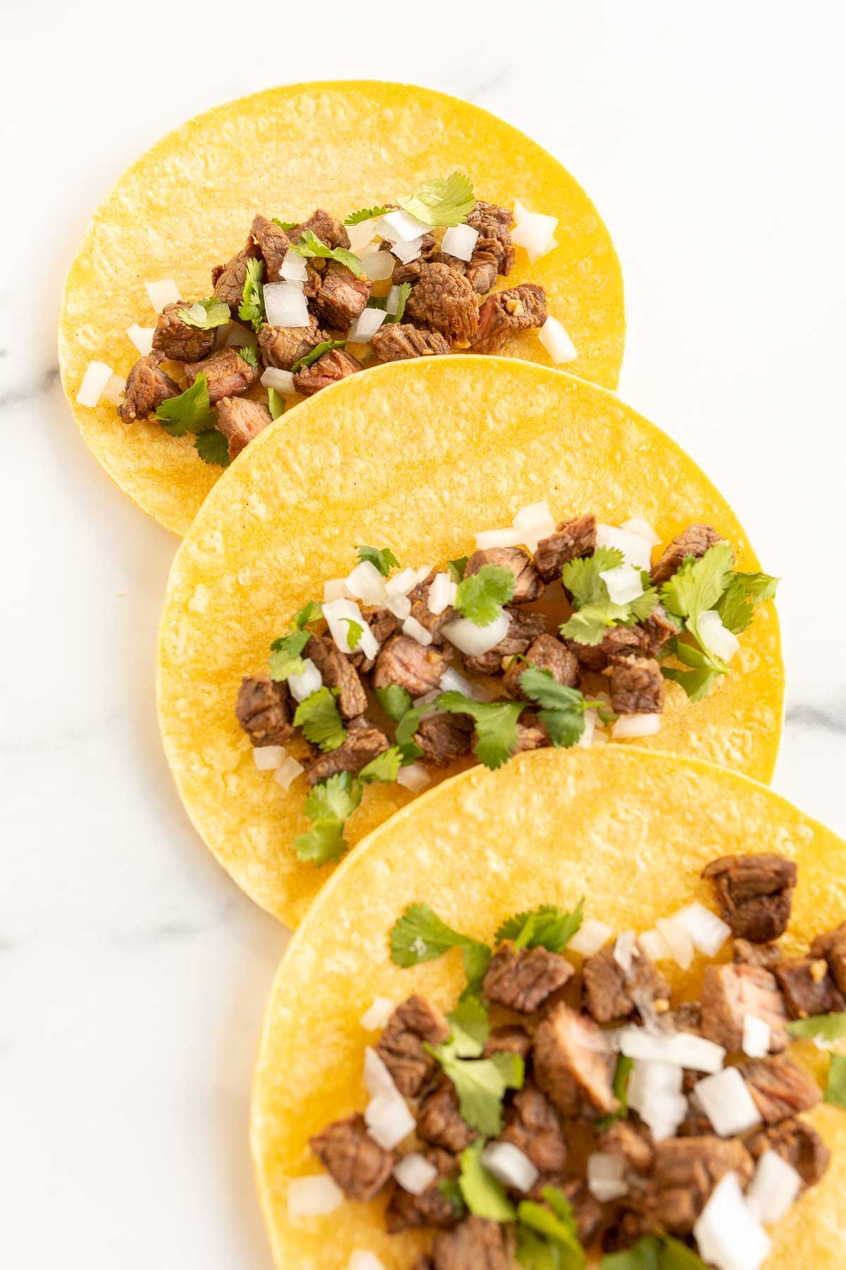 Carne asada street tacos in corn tortillas laid out flat on a marble surface