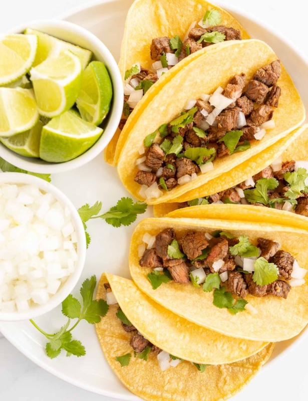 small tacos on a white platter with lime and onions for toppings