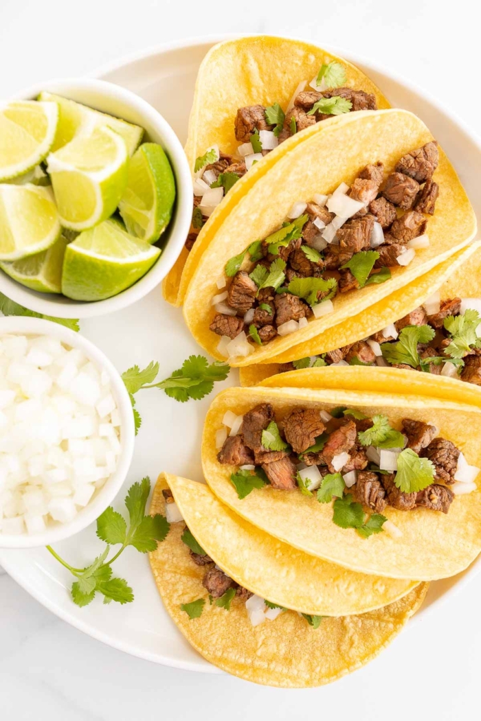 small tacos on a white platter with lime and onions for toppings