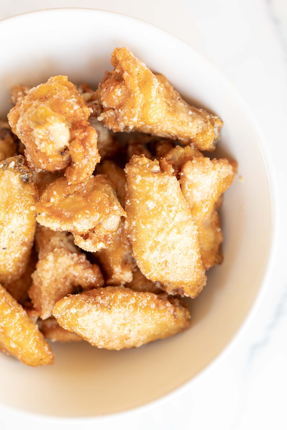 A white bowl filled with garlic parmesan wings, on a marble countertop