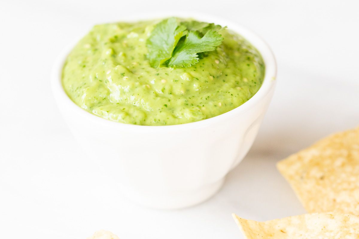 Salsa guacamole in a white bowl, tortilla chips scattered around