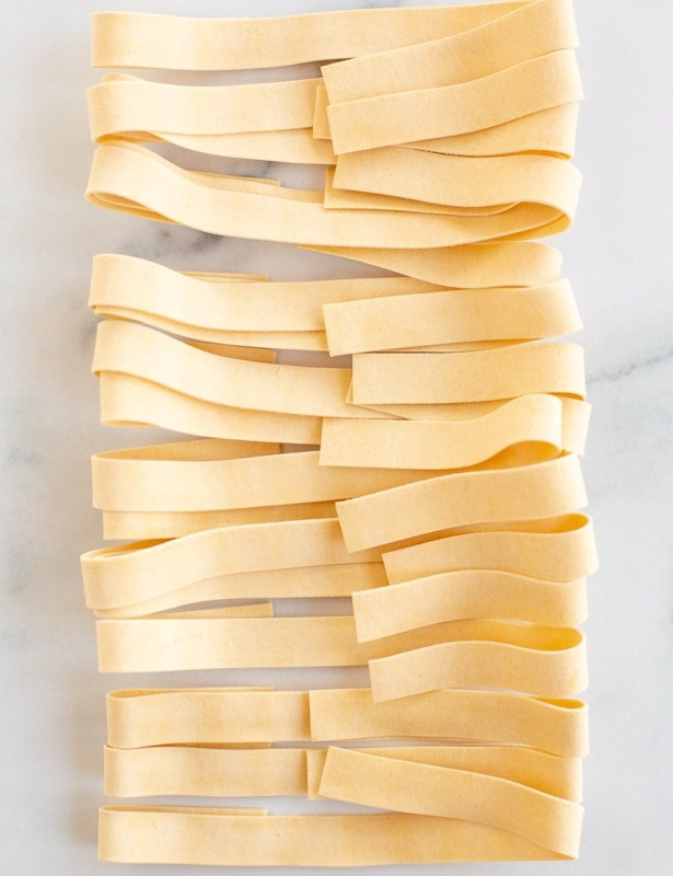 Strips of homemade Pappardelle pasta on a marble countertop