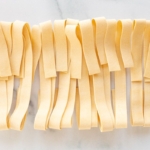 Strips of homemade dough cut into pappardelle and laid out on a marble surface, cut into strips for Pappardelle on a marble countertop
