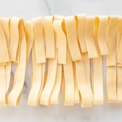 Strips of homemade dough cut into pappardelle and laid out on a marble surface, cut into strips for Pappardelle on a marble countertop