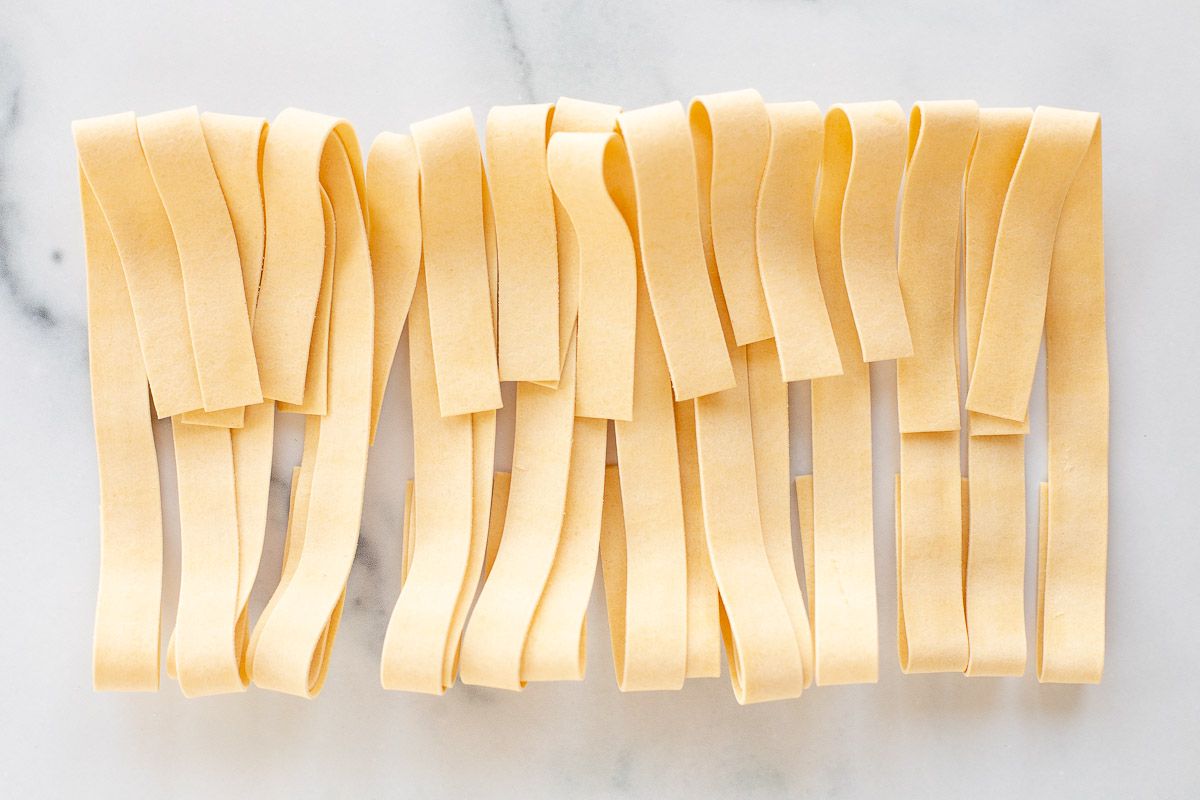 Strips of homemade Pappardelle on a marble countertop