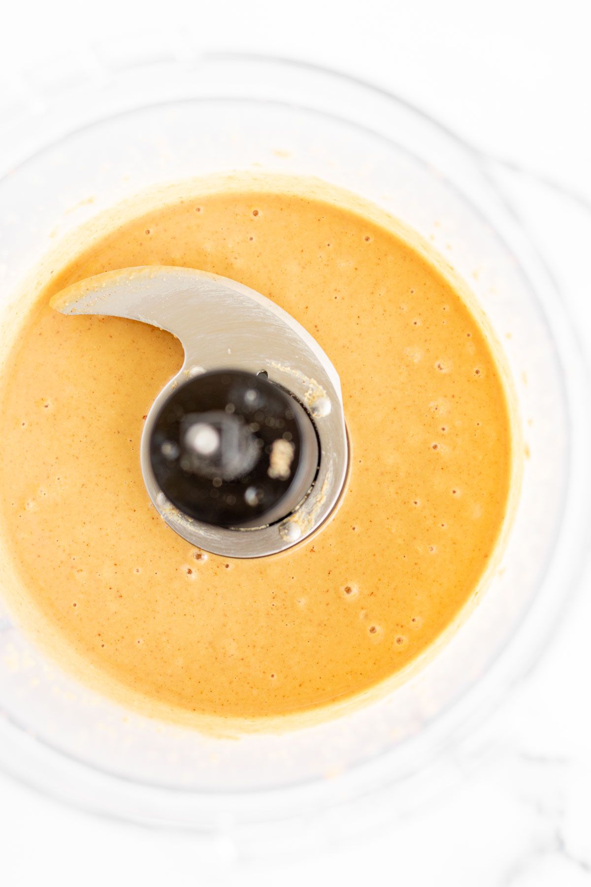 Image features homemade peanut butter in a food processor as part of a tutorial for how to make peanut butter.
