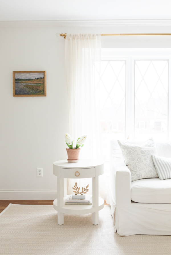 A white side table in a living room with a neutral sisal look indoor outdoor rug