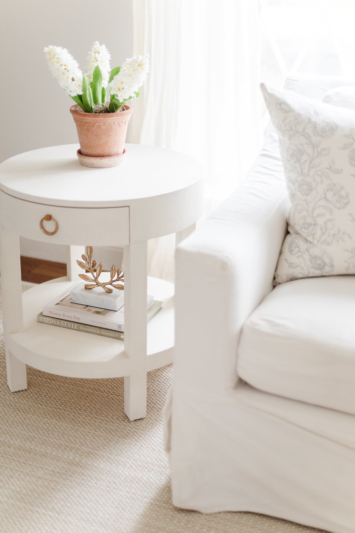 A white side table in a living room with a neutral sisal look indoor outdoor rug