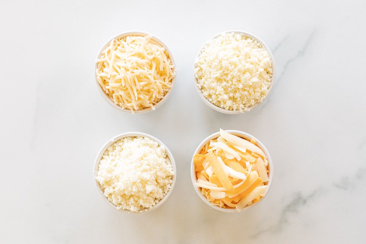 Four bowls of shredded Mexican cheese on a marble surface in a taste test of the best cheeses for tacos