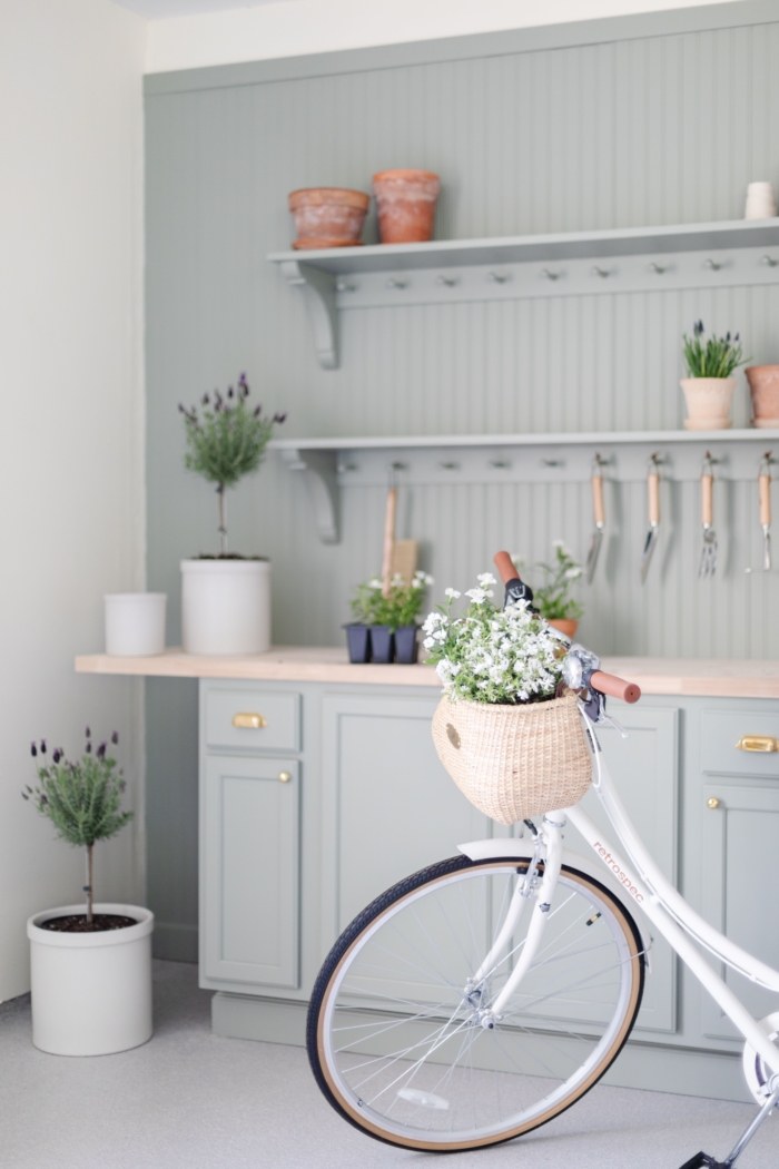 A green built in potting bench with garden tools and flowers, with a white bike in front