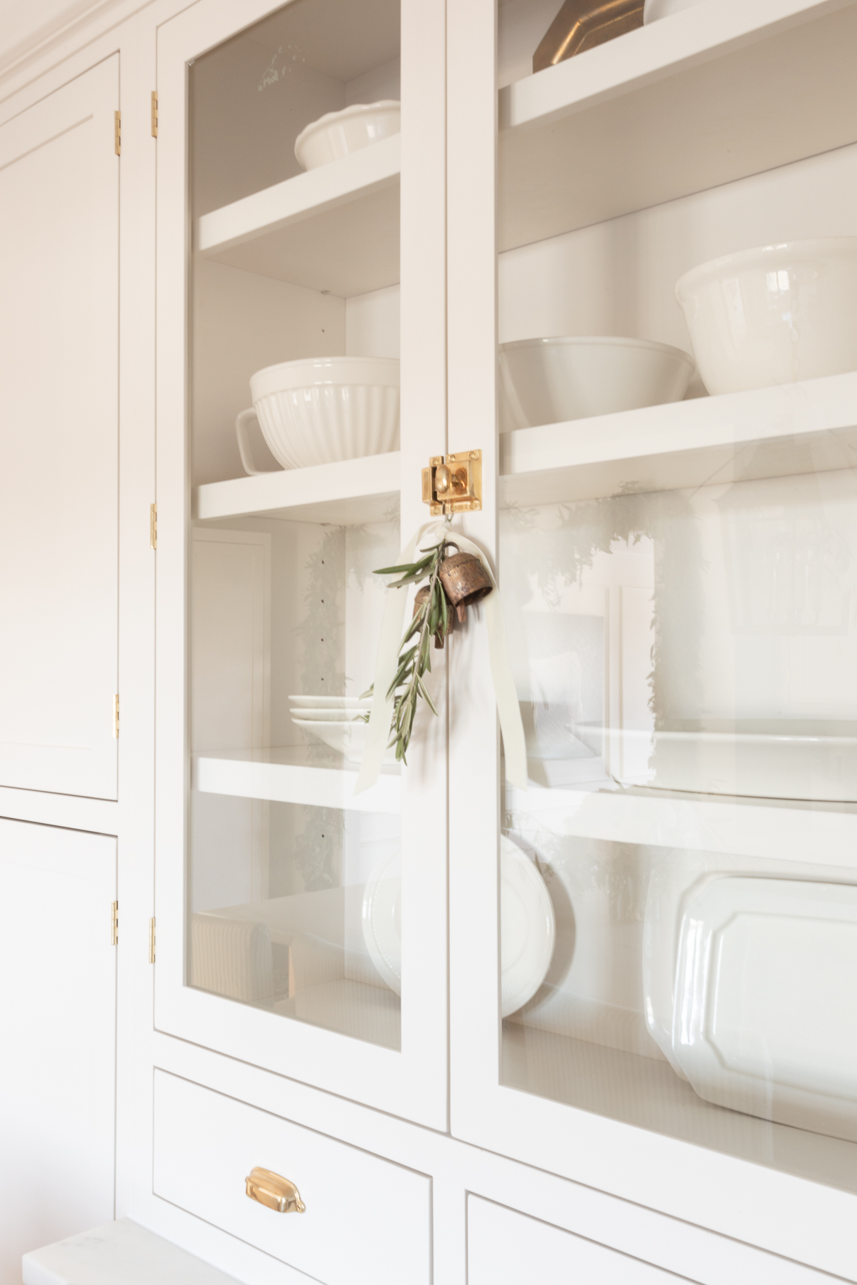 Glass shaker cabinets in a cream colored kitchen, brass hardware on the doors