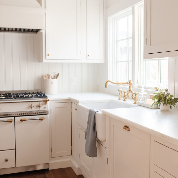 A white kitchen with shaker cabinets and marble counters, with a vase of flowers by the sink.