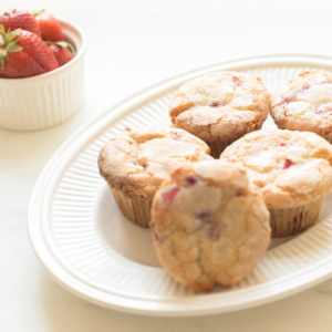 Strawberry muffins on a plate next to a bowl of strawberries, showcasing delicious strawberry recipes.