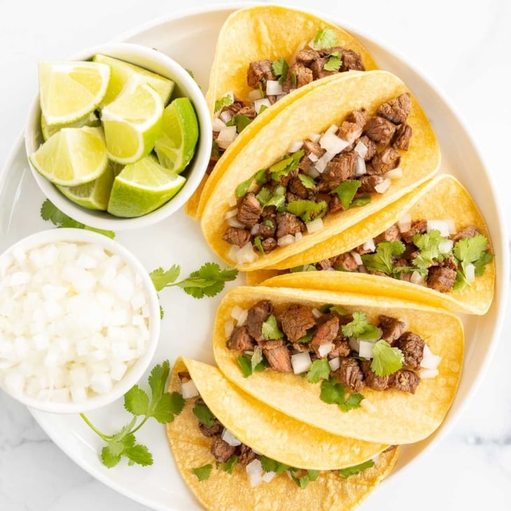 small tacos on a white platter with lime and onions for toppings