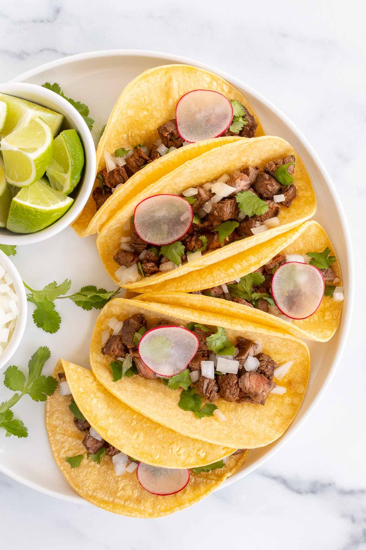 small tacos on a white platter with lime and onions for toppings