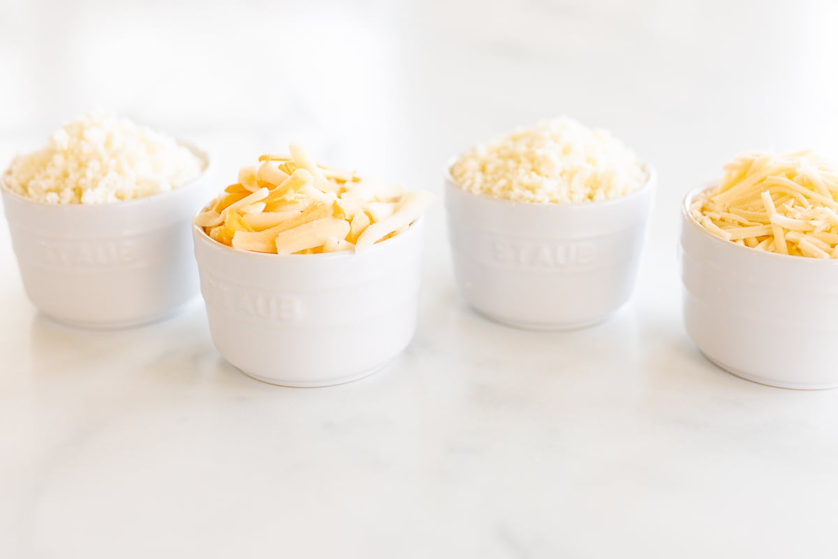 Four white cups filled with the best cheeses for tacos, including delicious Mexican cheese.