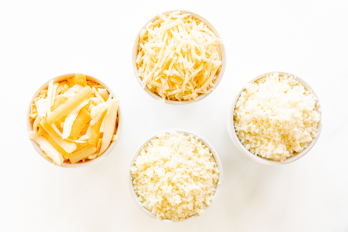 Four bowls of Mexican cheese on a white surface.