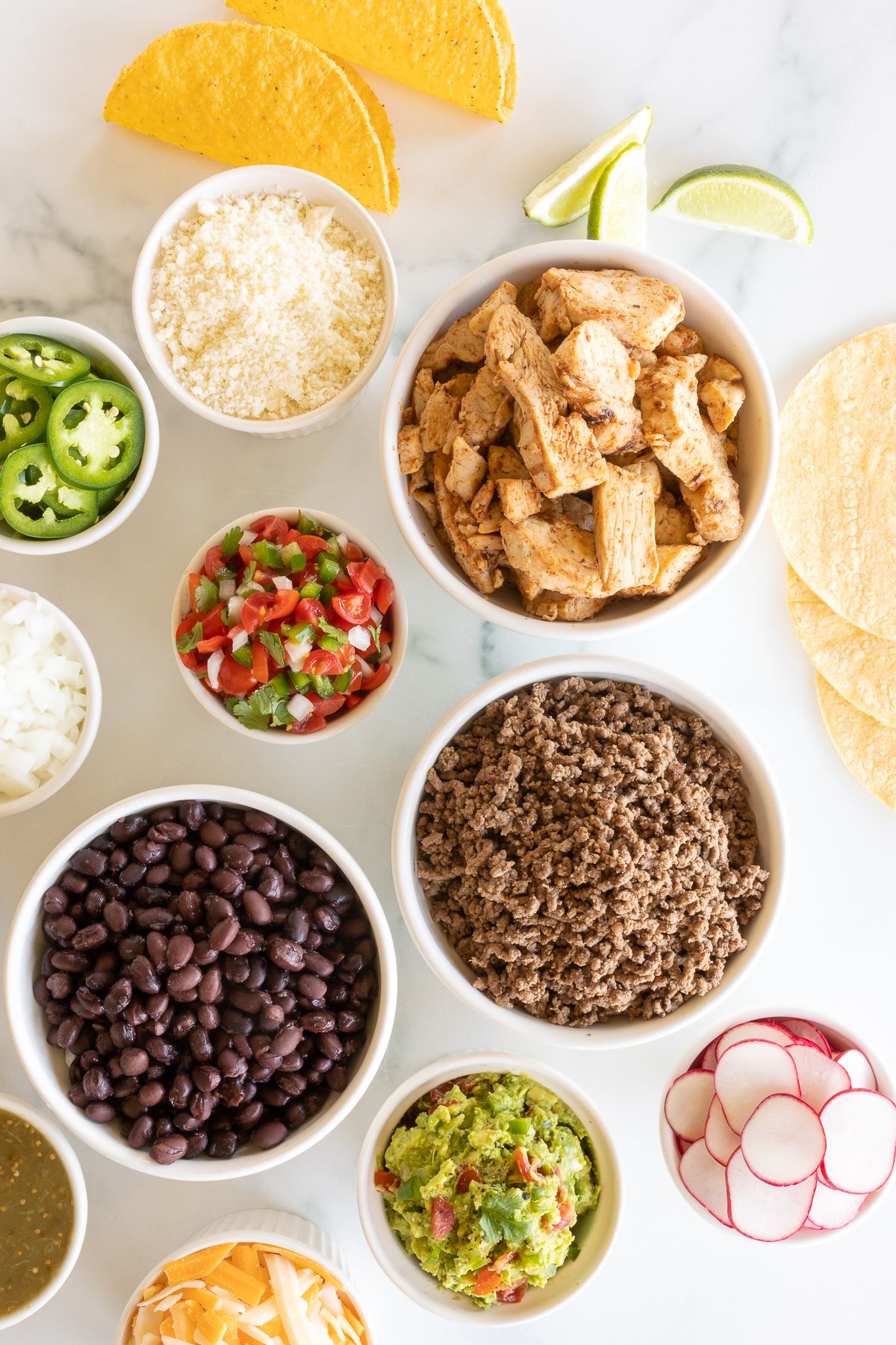 A display of taco toppings on a white marble countertop