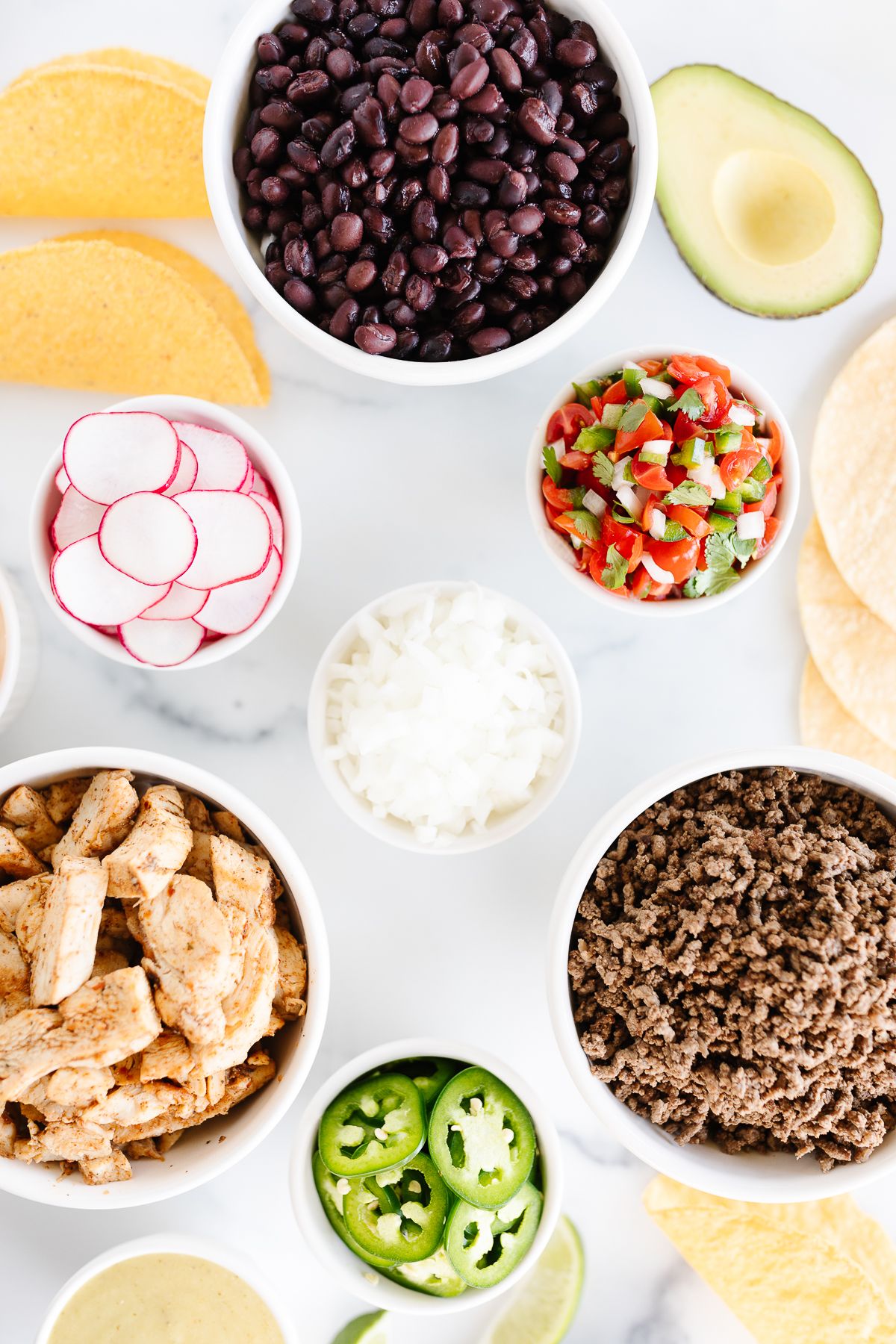 A display of taco toppings on a white marble countertop
