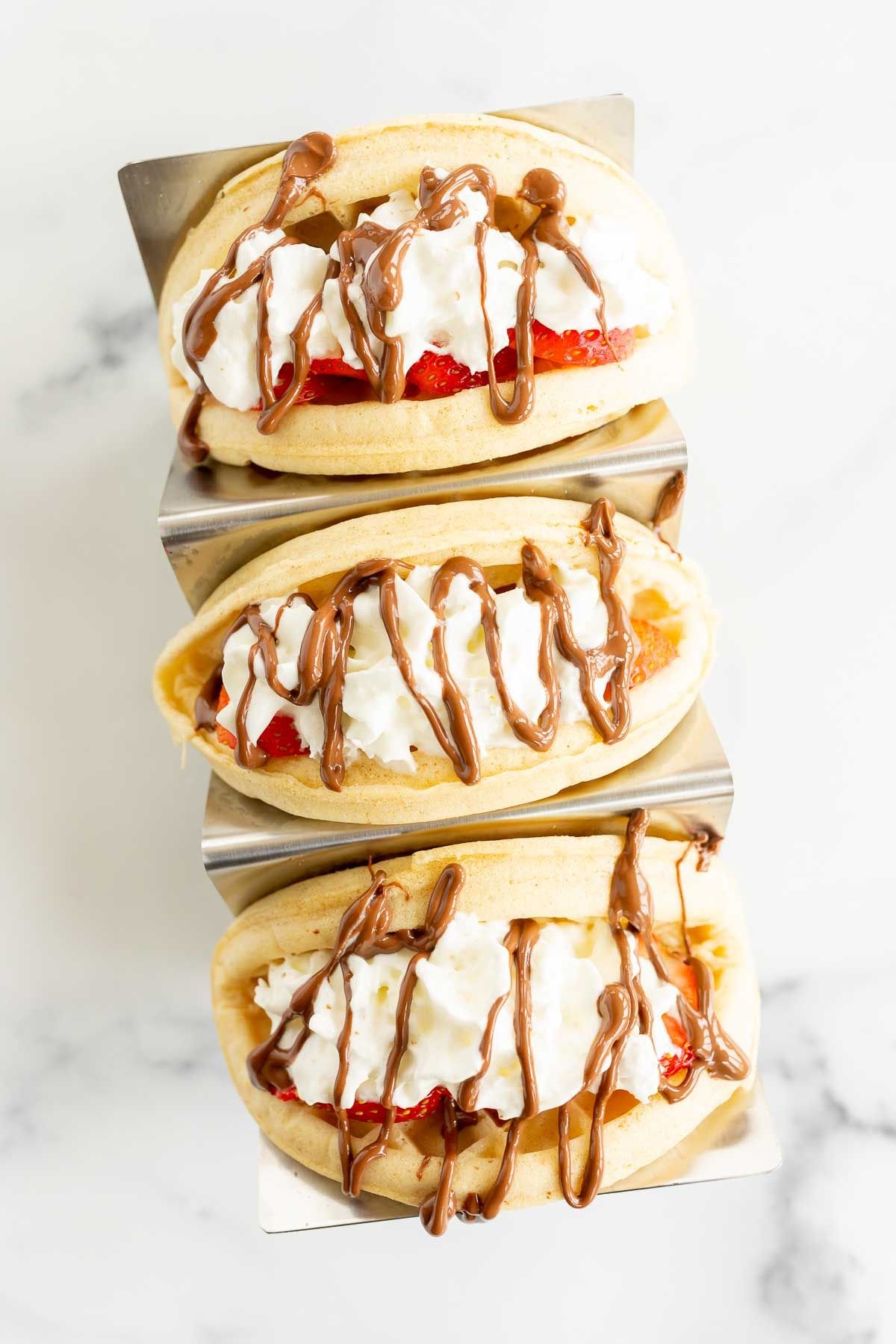 Waffle tacos on a stainless steel taco holder, filled with sweet ingredients