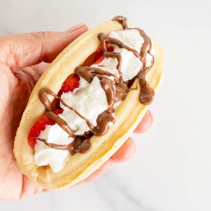 A waffle taco filled with strawberries, Nutella and whipped cream.